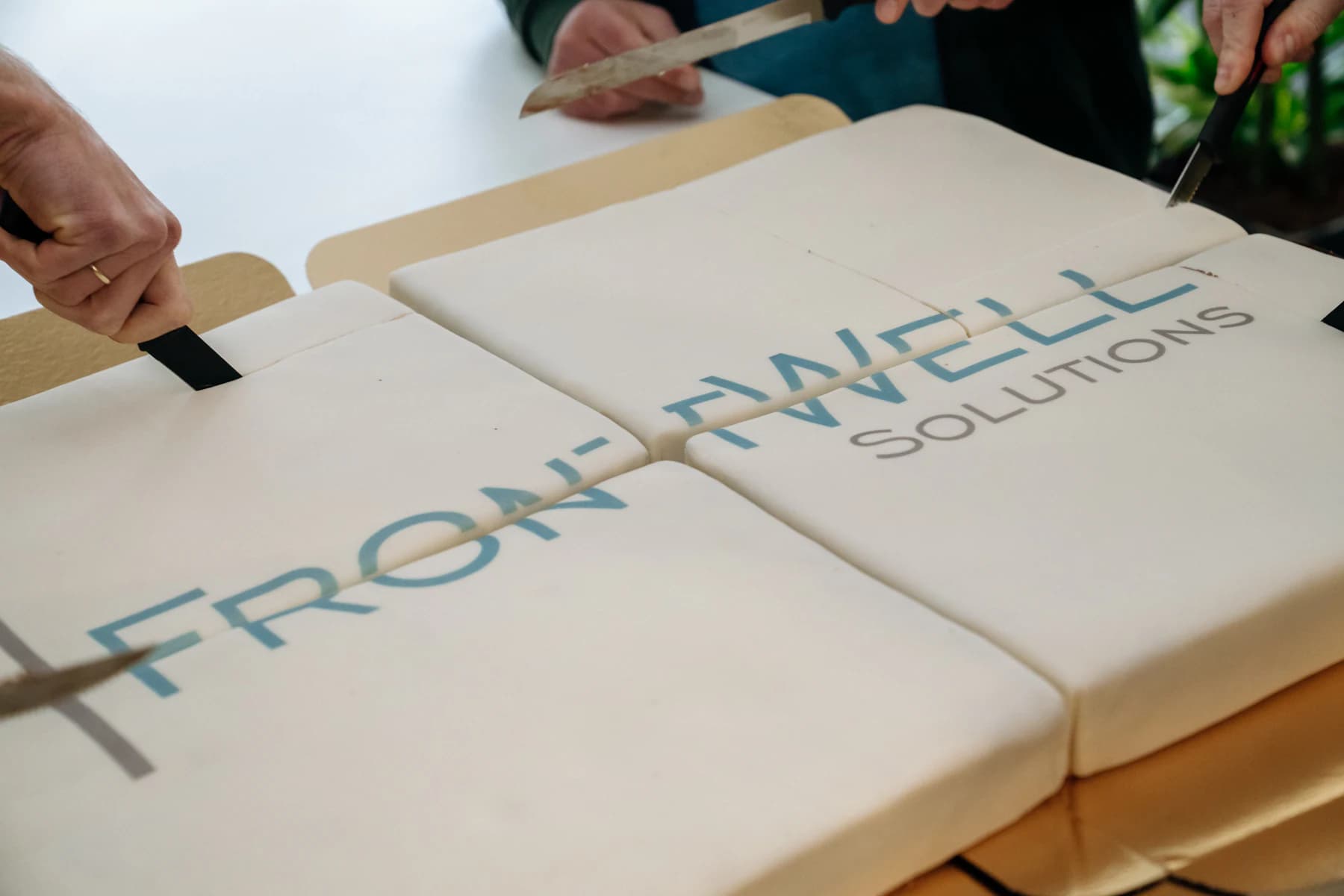 Several colleagues cutting a FrontWell Solutions celebration cake together.